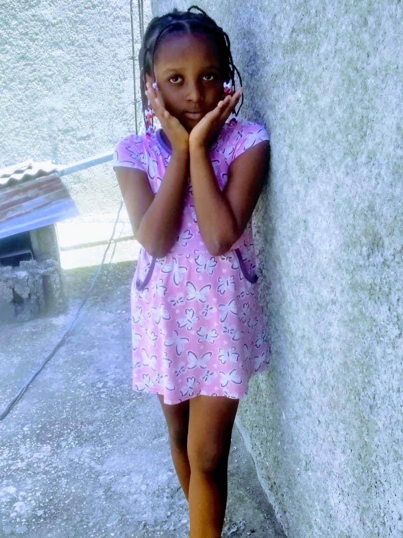 Petite fille en robe rose posant devant le mur de sa maison