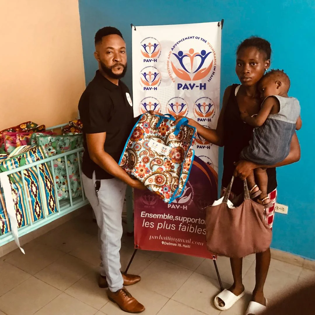PAV-H member handing a kit to a young mother carrying her baby