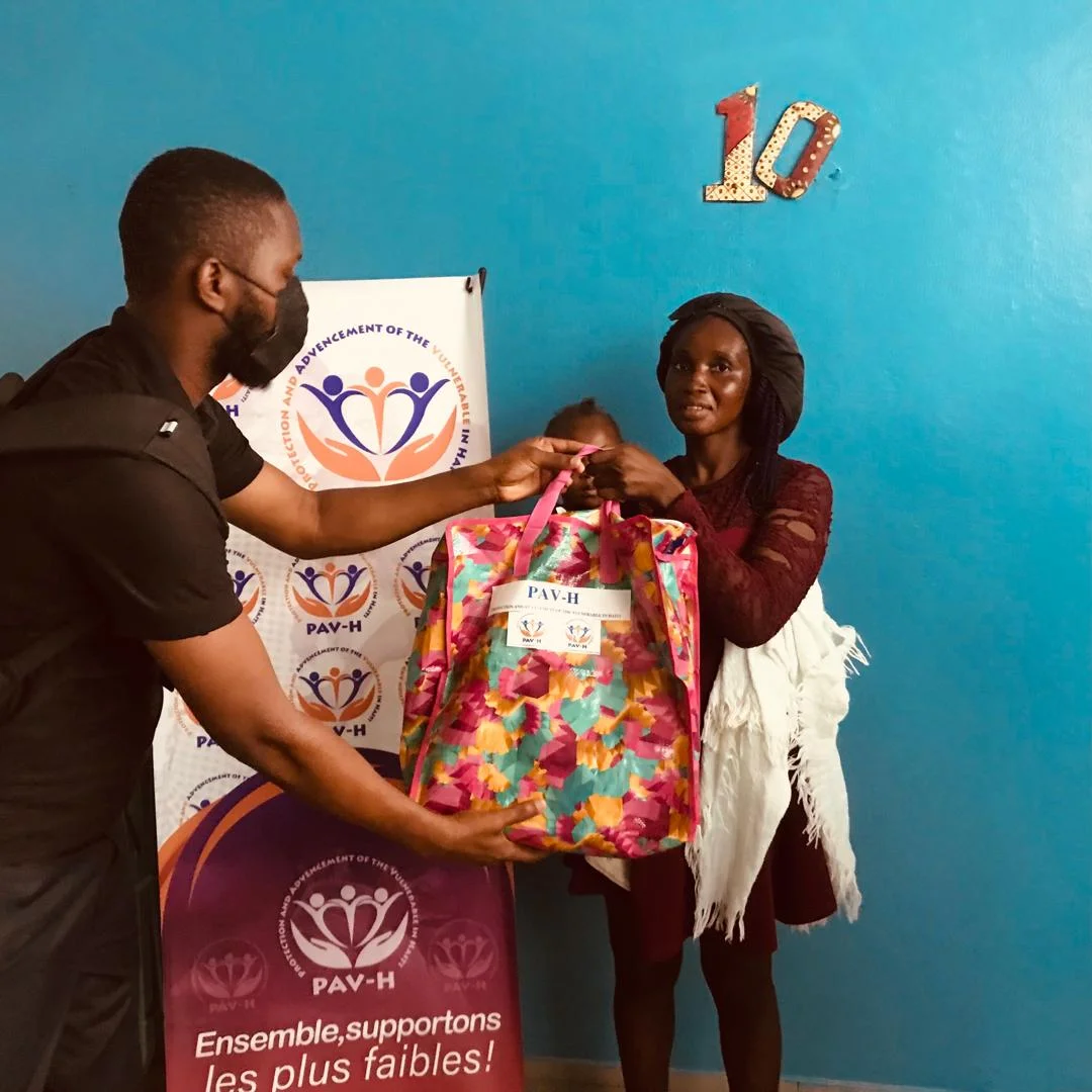 PAV-H volunteer handing a colorful bag to a mother with her child