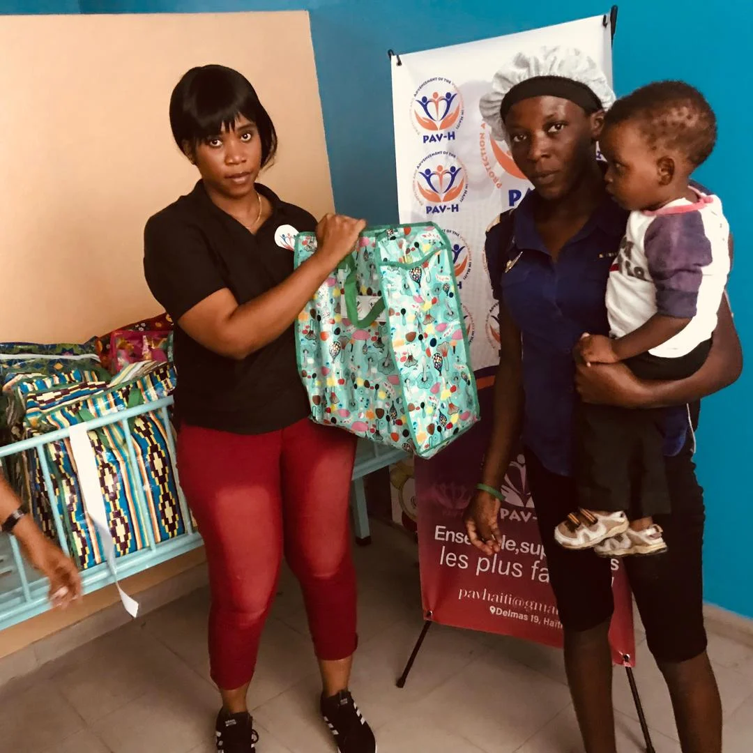Bénévole PAV-H remettant un sac à une maman portant son enfant