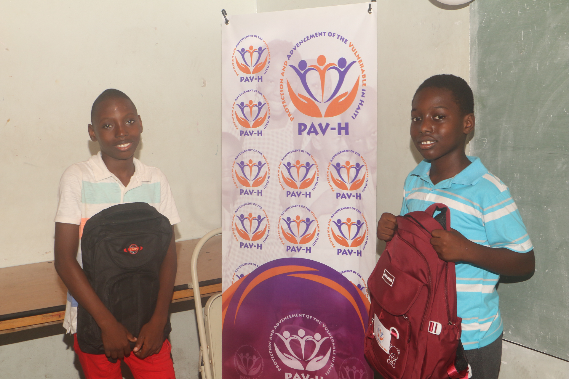 Two young boys with their new backpacks in front of the PAV-H banner