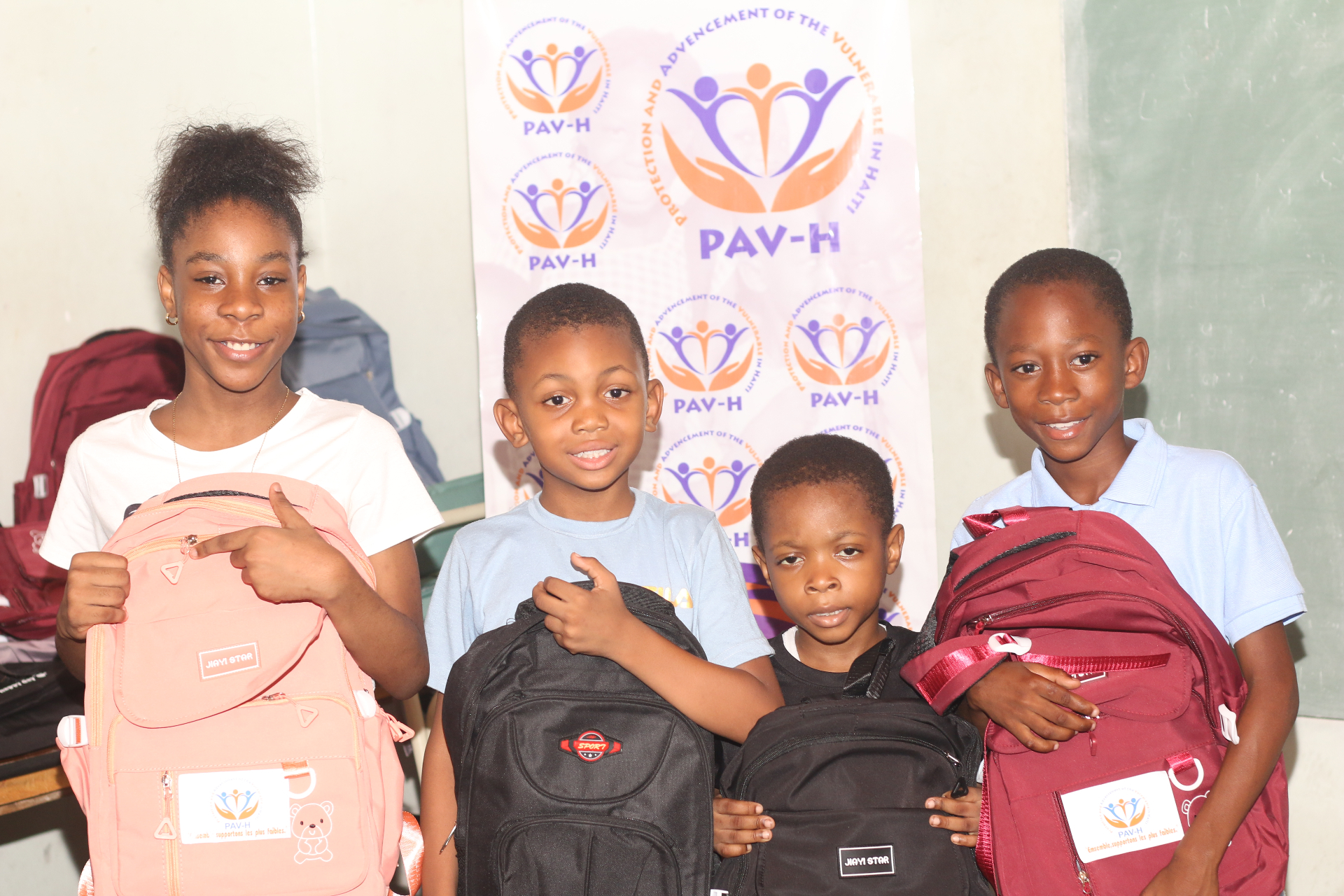 Four children proudly holding backpacks distributed by PAV-H